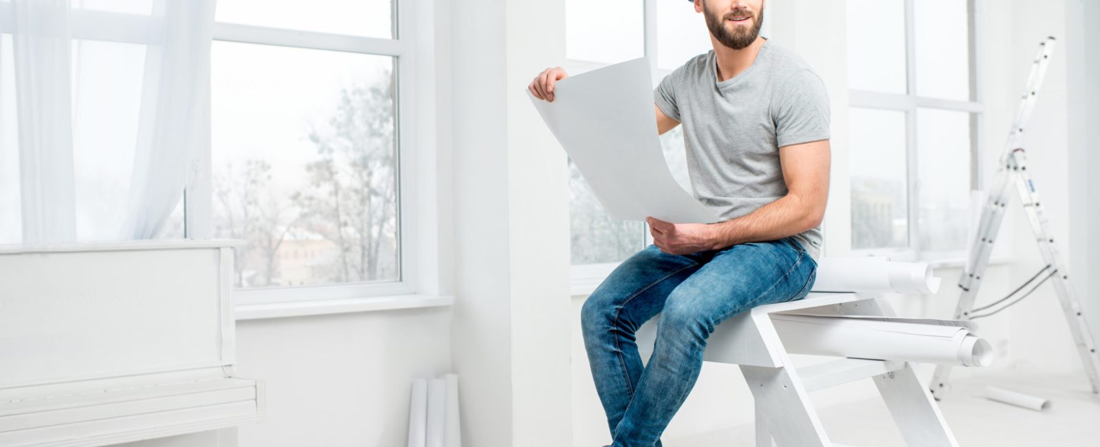 Handsome repairman or builder in helmet working with drawings on renovation of apartment interior
