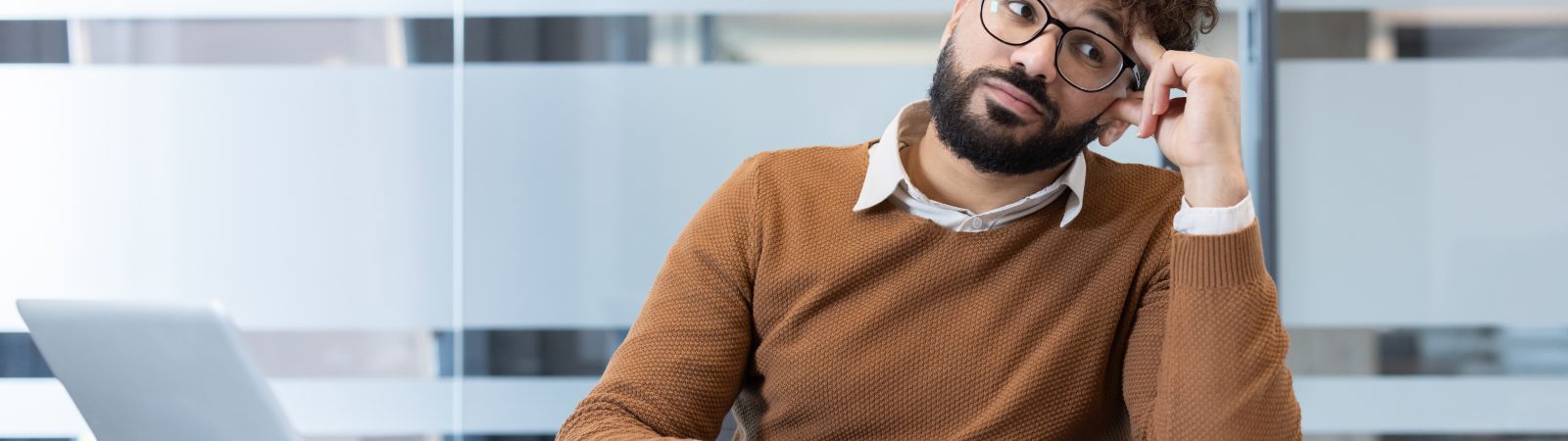 Man experiencing mental block at office desk, surrounded by crumpled paper, laptop, and documents, highlighting stress, challenge, and creative struggle in the workspace