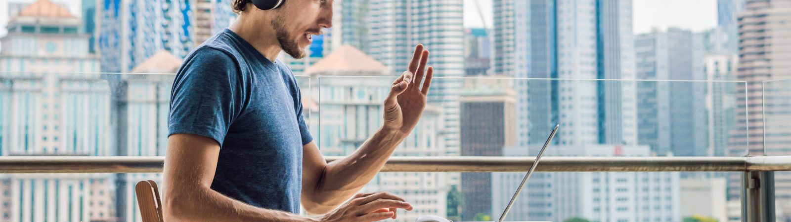 Young man teaches a foreign language or learns a foreign language on the Internet on her balcony against the backdrop of a big city. Online language school lifestyle. BANNER, long format