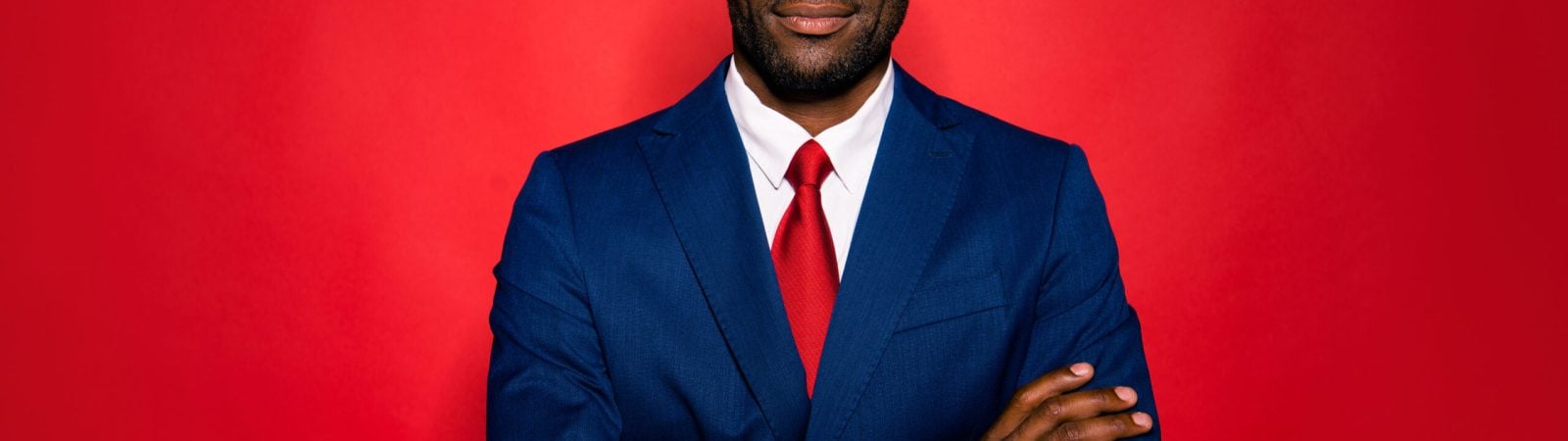 Portrait of nice positive calm experienced smart clever well-groomed attractive handsome content mulatto man folded arms in suit isolated over bright vivid red background
