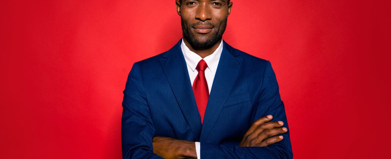Portrait of nice positive calm experienced smart clever well-groomed attractive handsome content mulatto man folded arms in suit isolated over bright vivid red background