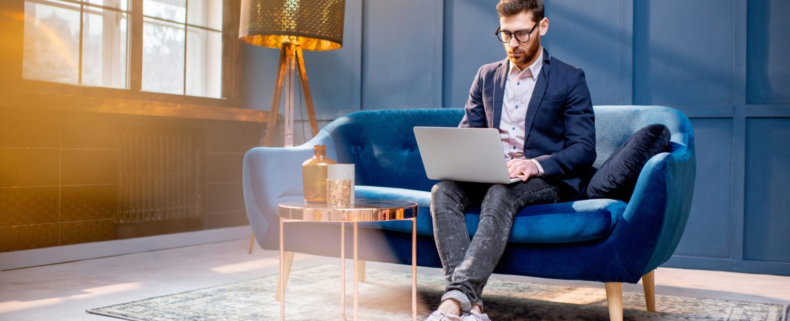 Portrait of an elegant businessman sitting with laptop on the couch at the luxury blue office interior