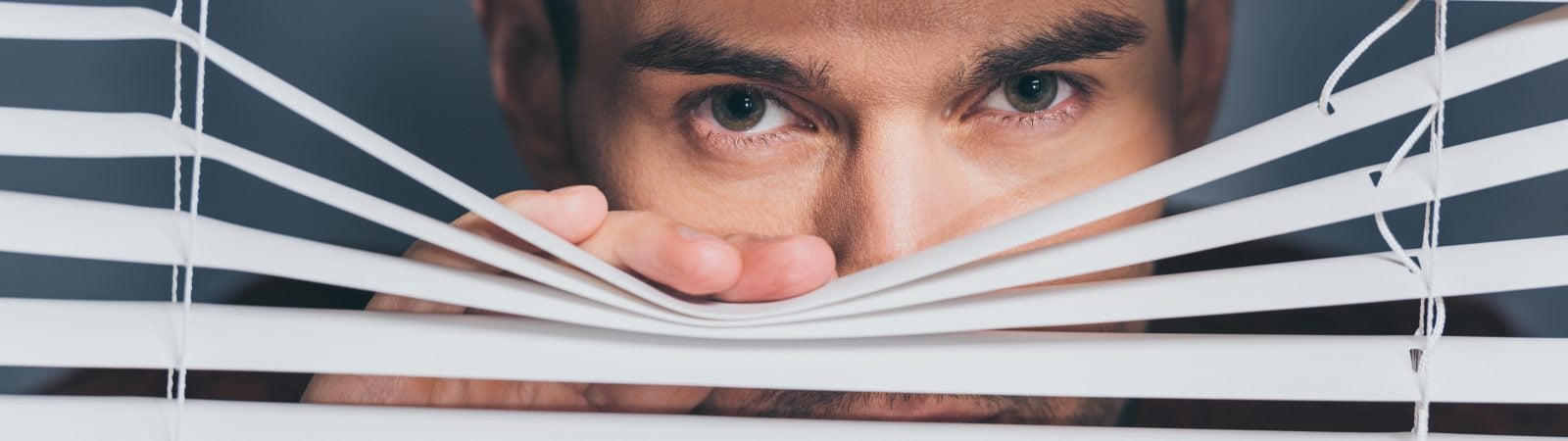 suspicious young man looking at camera through blinds, mistrust concept