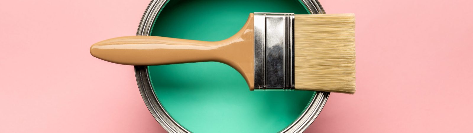 top view of tin of green paint and brush on pink surface