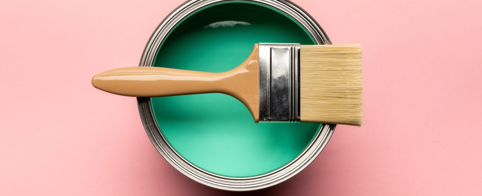 top view of tin of green paint and brush on pink surface