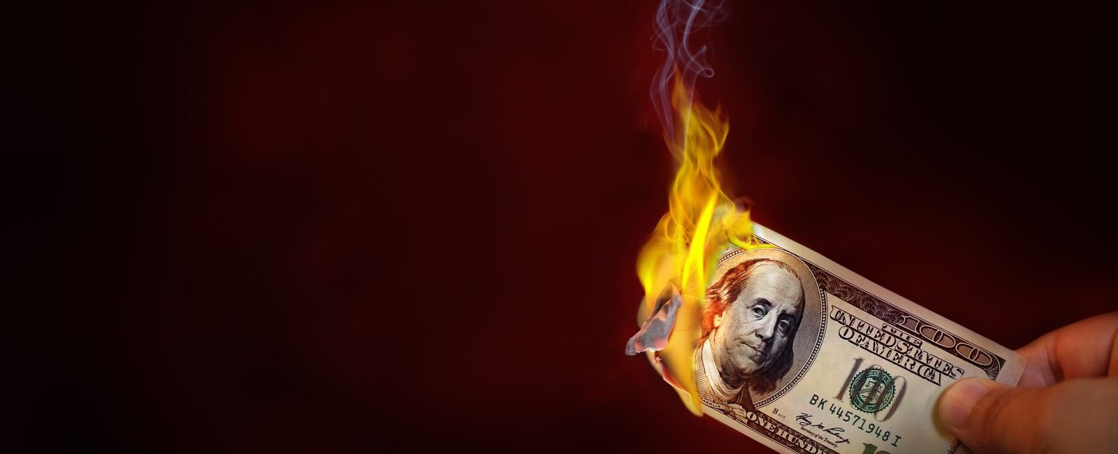 Hand holding a burning 100 dollar bill money with copy space.