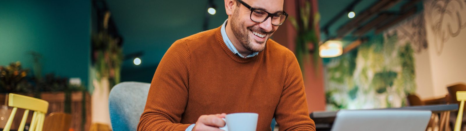 Freelancer working on laptop in a cafe, smiling and drinking coffee, portrait.