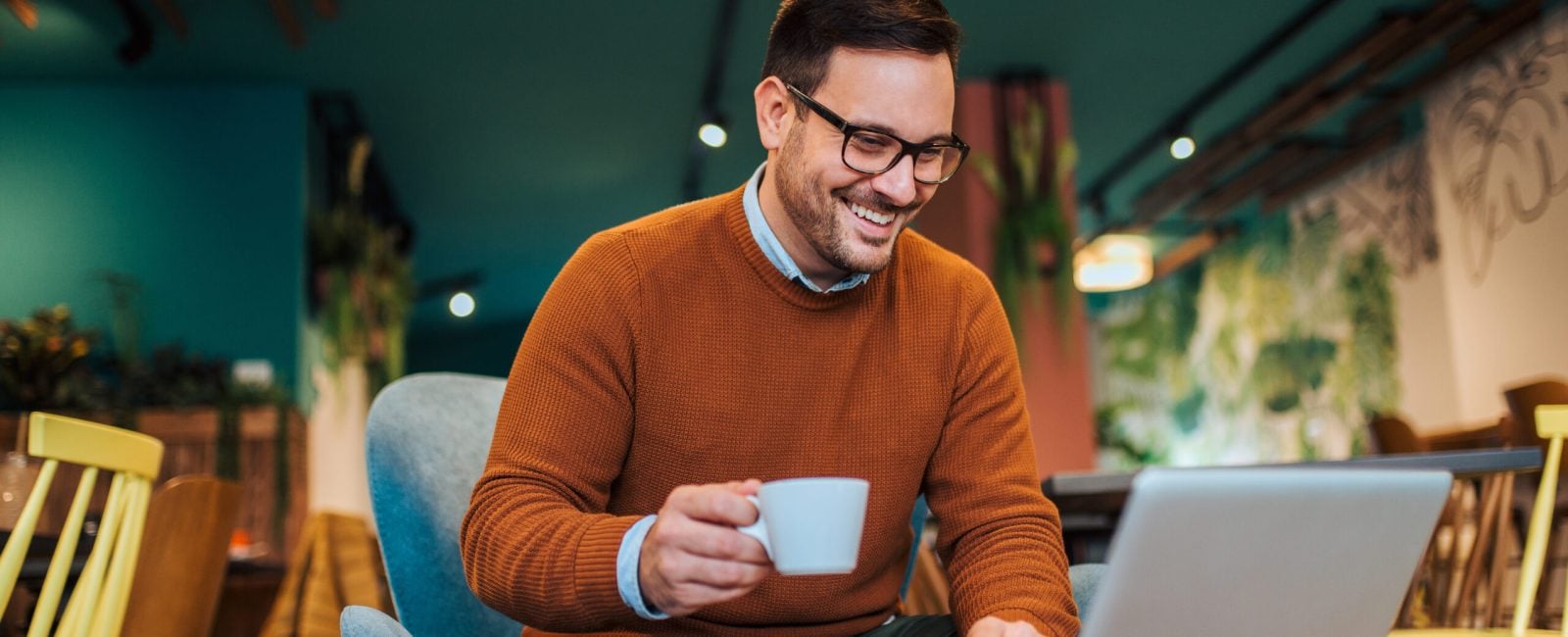 Freelancer working on laptop in a cafe, smiling and drinking coffee, portrait.