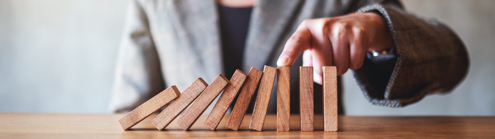 Closeup image of a businesswoman try to use finger to stop falling wooden dominoes blocks for business solution concept