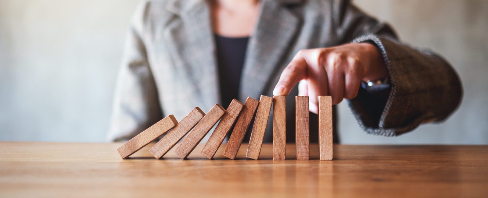 Closeup image of a businesswoman try to use finger to stop falling wooden dominoes blocks for business solution concept