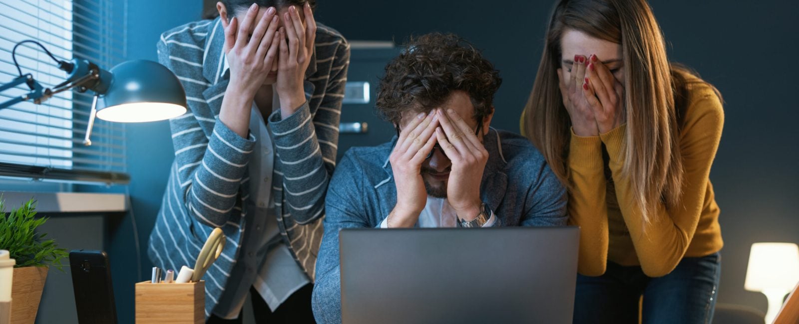 Young business team working with a laptop and experiencing problems, they are covering their faces with hands