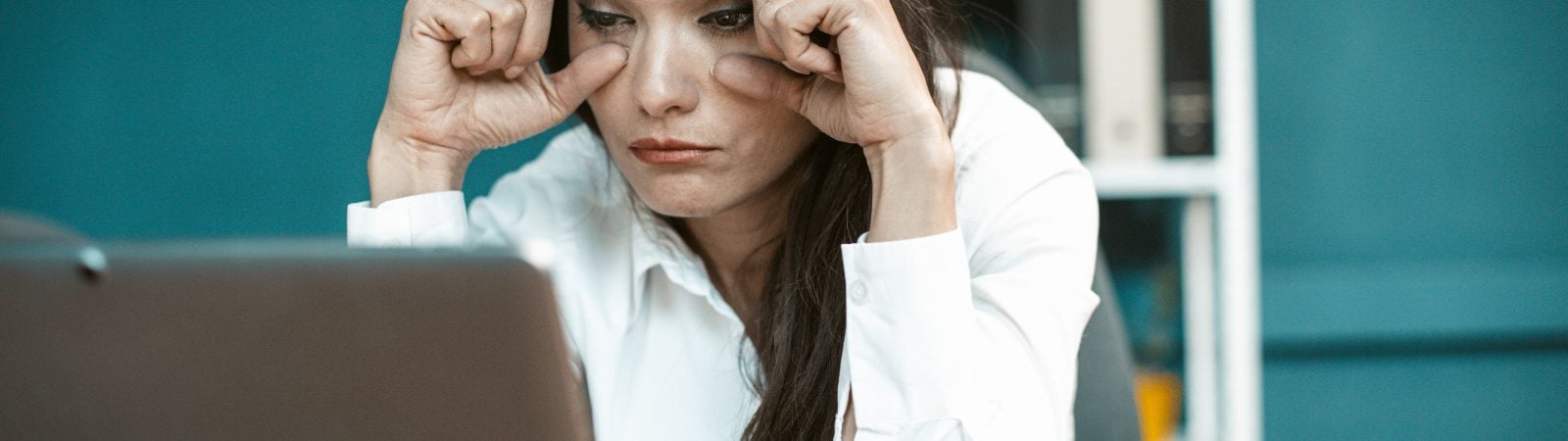 Overwork concept. Sleepy business woman in office. Tired Caucasian woman trying not to fall asleep while working on computer. She holding eyes with hands. Tinted image.