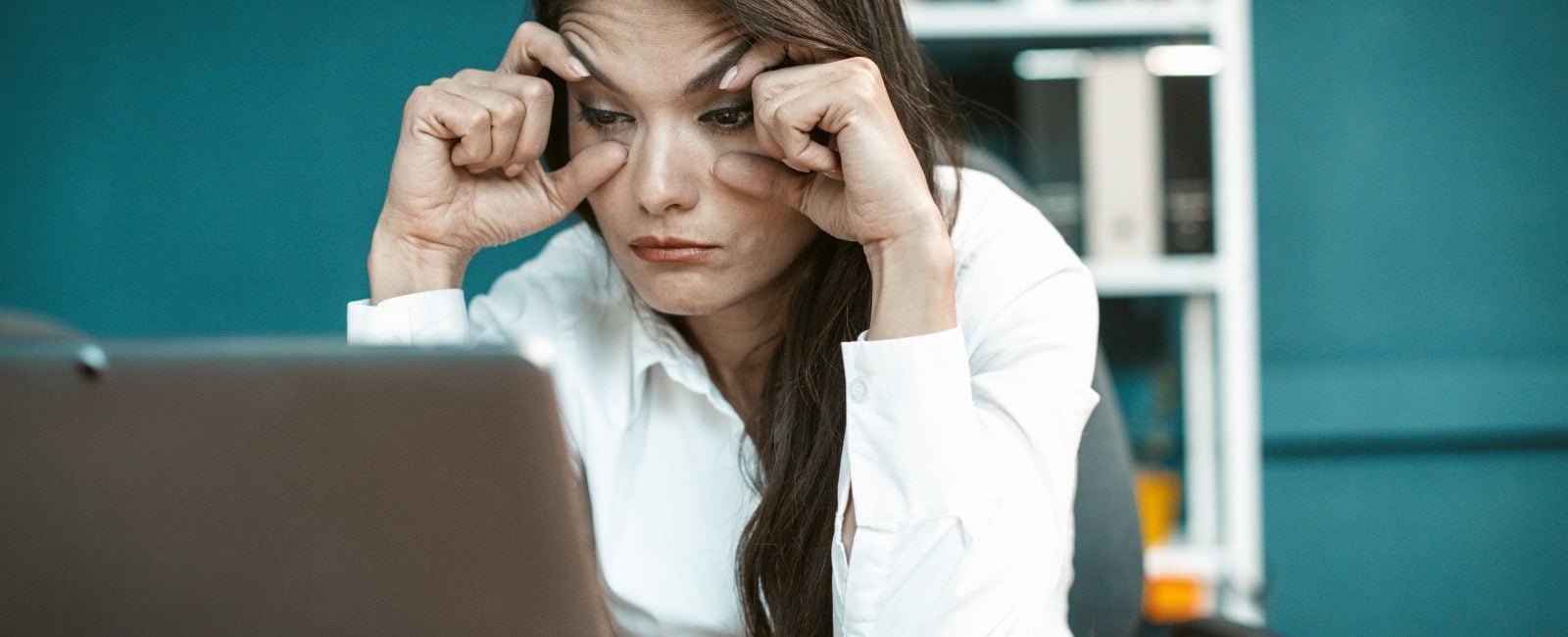 Overwork concept. Sleepy business woman in office. Tired Caucasian woman trying not to fall asleep while working on computer. She holding eyes with hands. Tinted image.