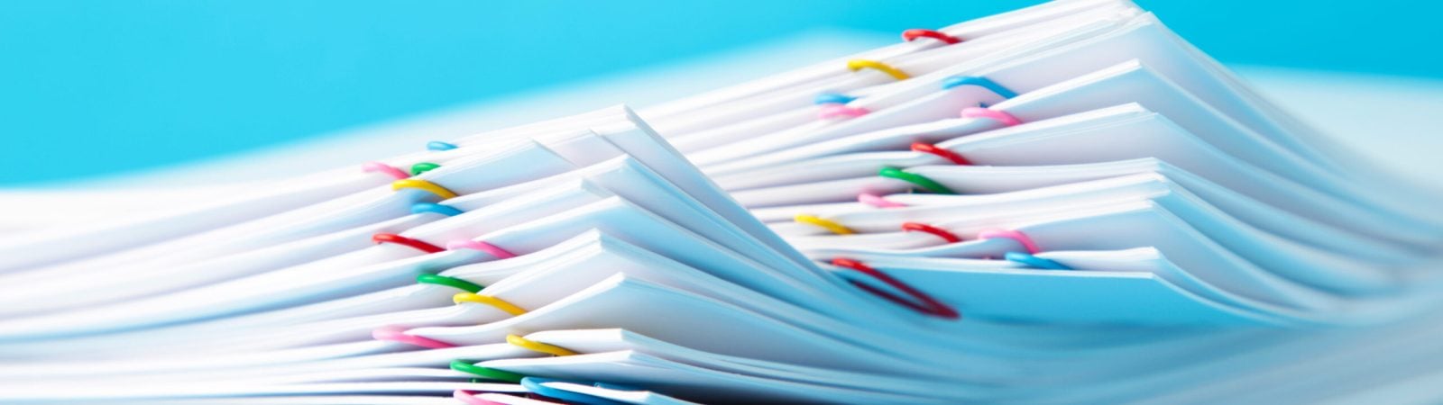 Colorful paper clip with pile of overload white paperwork on blue. Top view