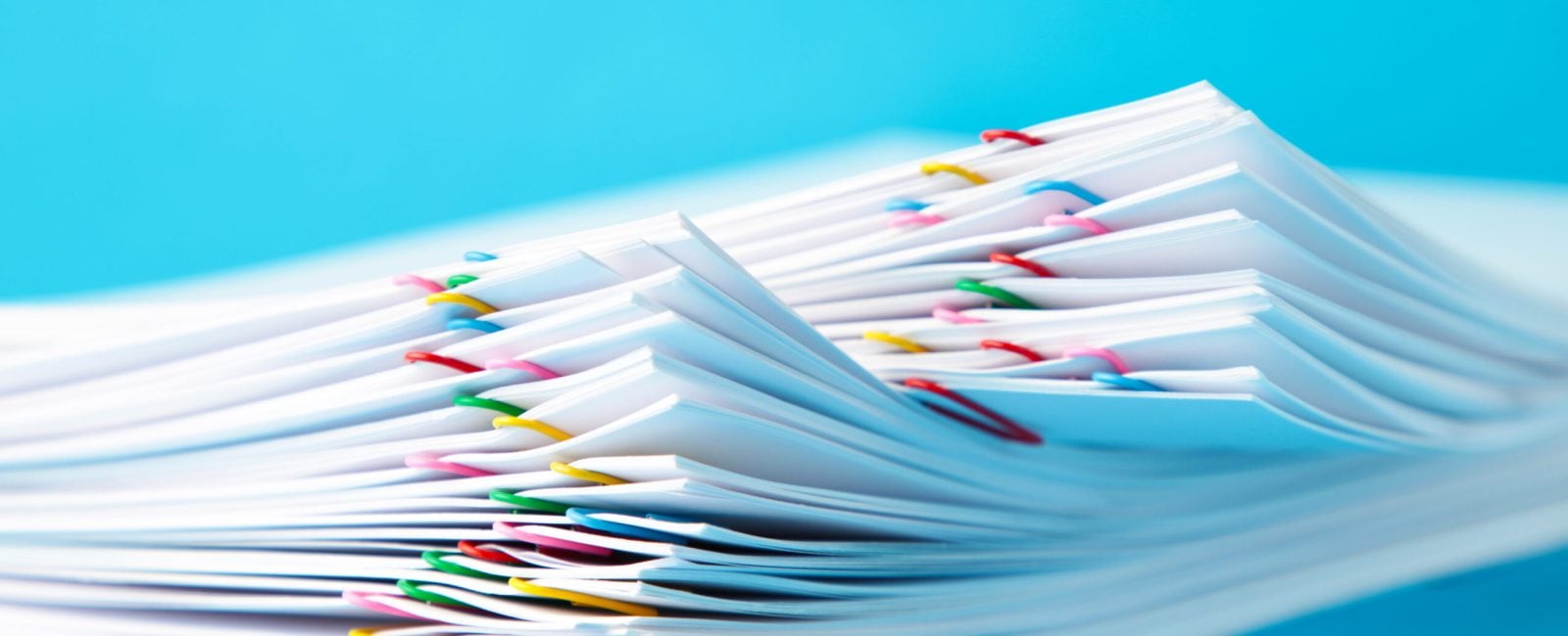 Colorful paper clip with pile of overload white paperwork on blue. Top view