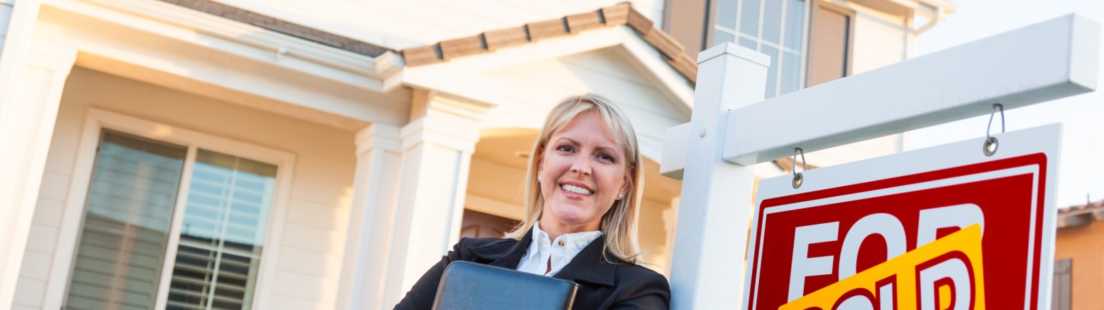 Female Real Estate Agent in Front of Sold For Sale Sign and Beautiful House.