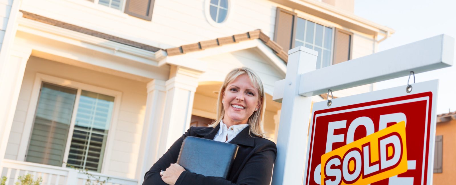 Female Real Estate Agent in Front of Sold For Sale Sign and Beautiful House.