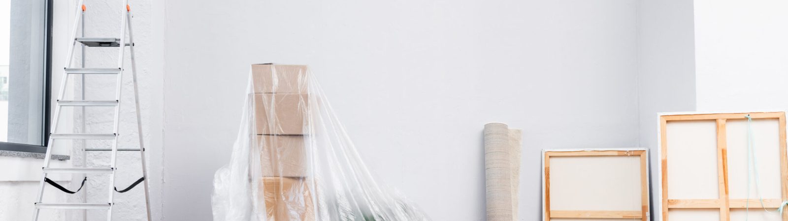 interior of room with ladder, cardboard boxes covered with polyethylene, pictures and equipment for repair