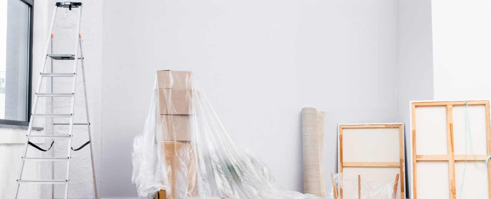 interior of room with ladder, cardboard boxes covered with polyethylene, pictures and equipment for repair