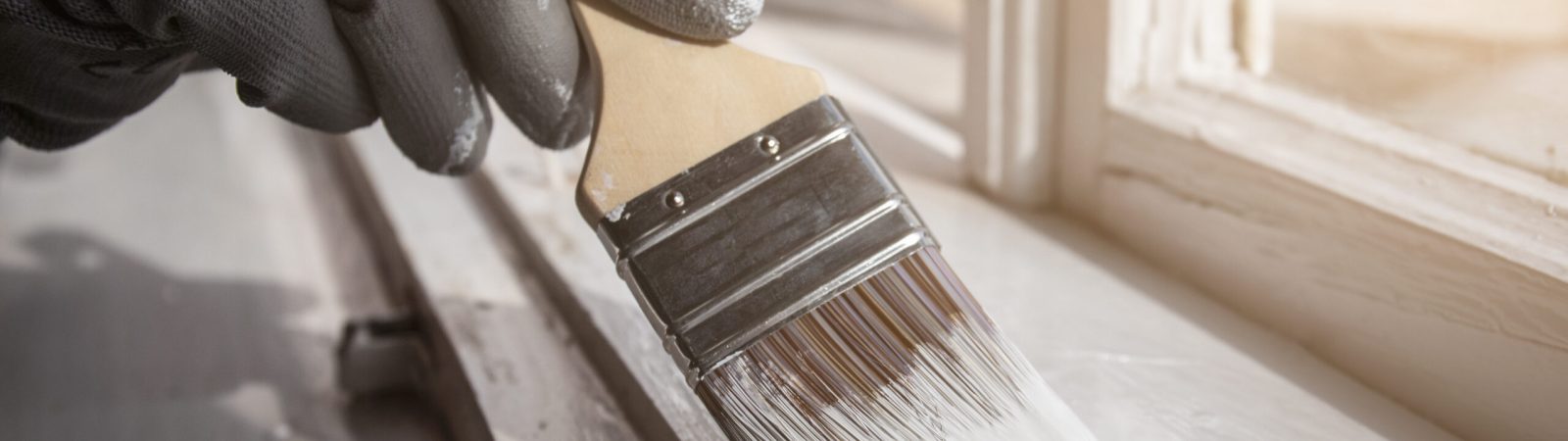 Painting wooden window with white color. Brush in hand with grey glove. Ronoveation and restauration.