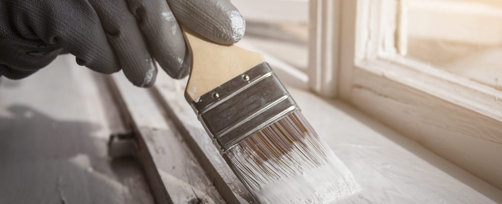 Painting wooden window with white color. Brush in hand with grey glove. Ronoveation and restauration.
