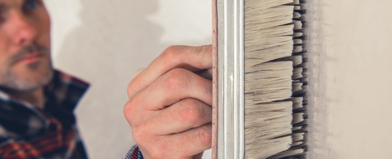 Caucasian Worker in His 40s Walls Priming Using Large Painting Brush Close Up. Refreshing Apartment Interiors. Home Remodeling Theme.