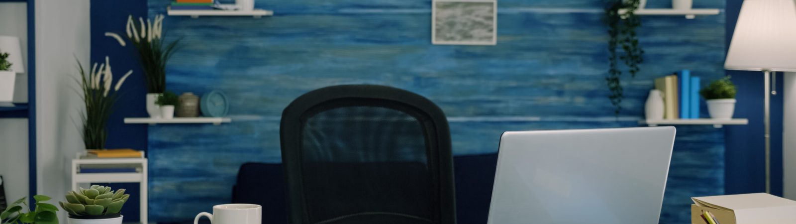 Empty workspace of freelancer worker with laptop computer on desk and cup of coffee. Interior of empty bright workspace with blue furniture and walls, beautiful decorated, cozy apartment