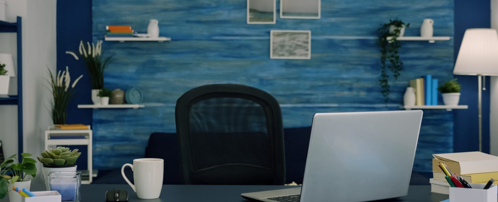 Empty workspace of freelancer worker with laptop computer on desk and cup of coffee. Interior of empty bright workspace with blue furniture and walls, beautiful decorated, cozy apartment