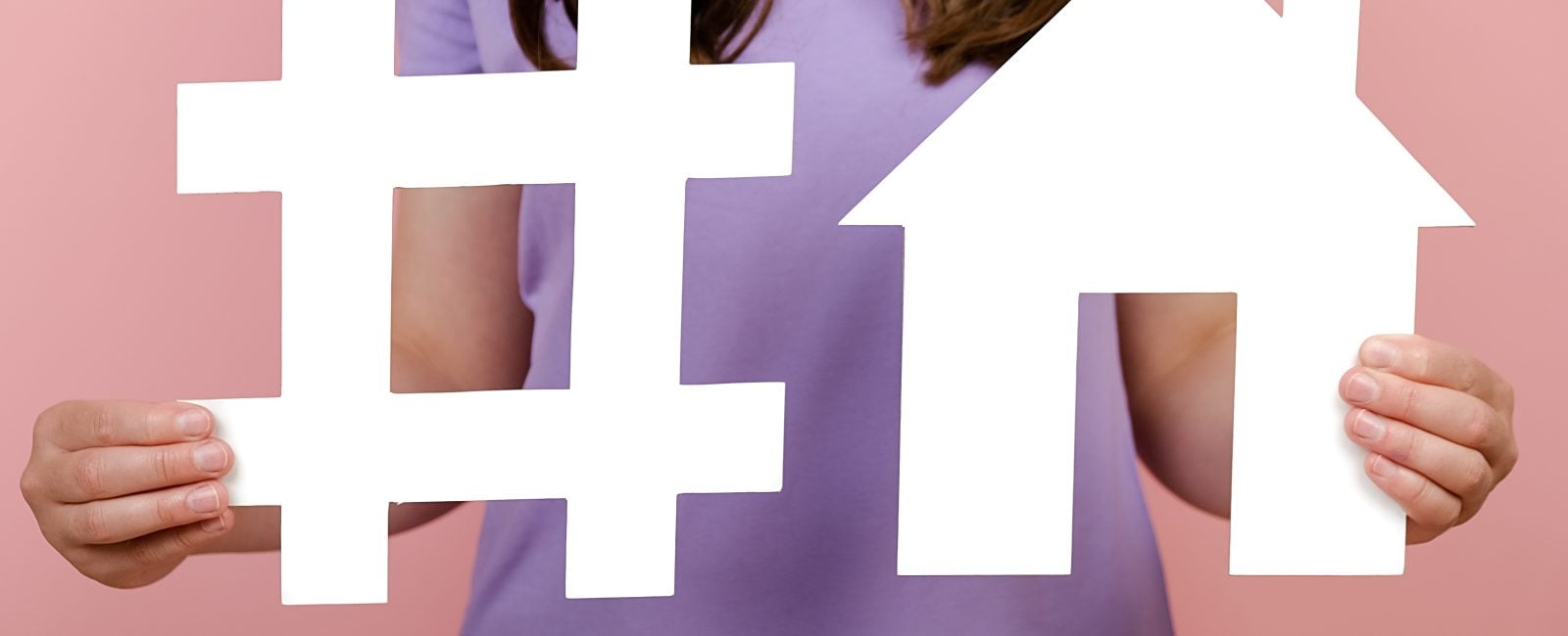 Closeup of unrecognizable woman holds white hashtag sign and house model, label for business, marketing, advertising, isolated on pink wall. Social network monitoring, media measurement, mortgage