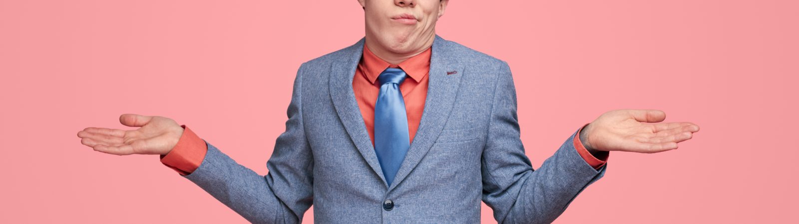 Funny clueless male entrepreneur in suit shrugging shoulders and expressing misunderstanding on pink background in studio while looking at camera