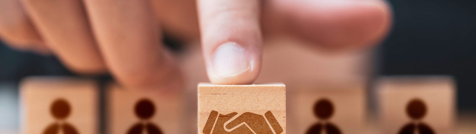 Hand putting hand shaking which print screen on wooden cube block  in front of human icon for business deal and agreement concept.