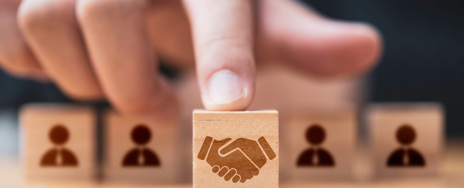 Hand putting hand shaking which print screen on wooden cube block  in front of human icon for business deal and agreement concept.