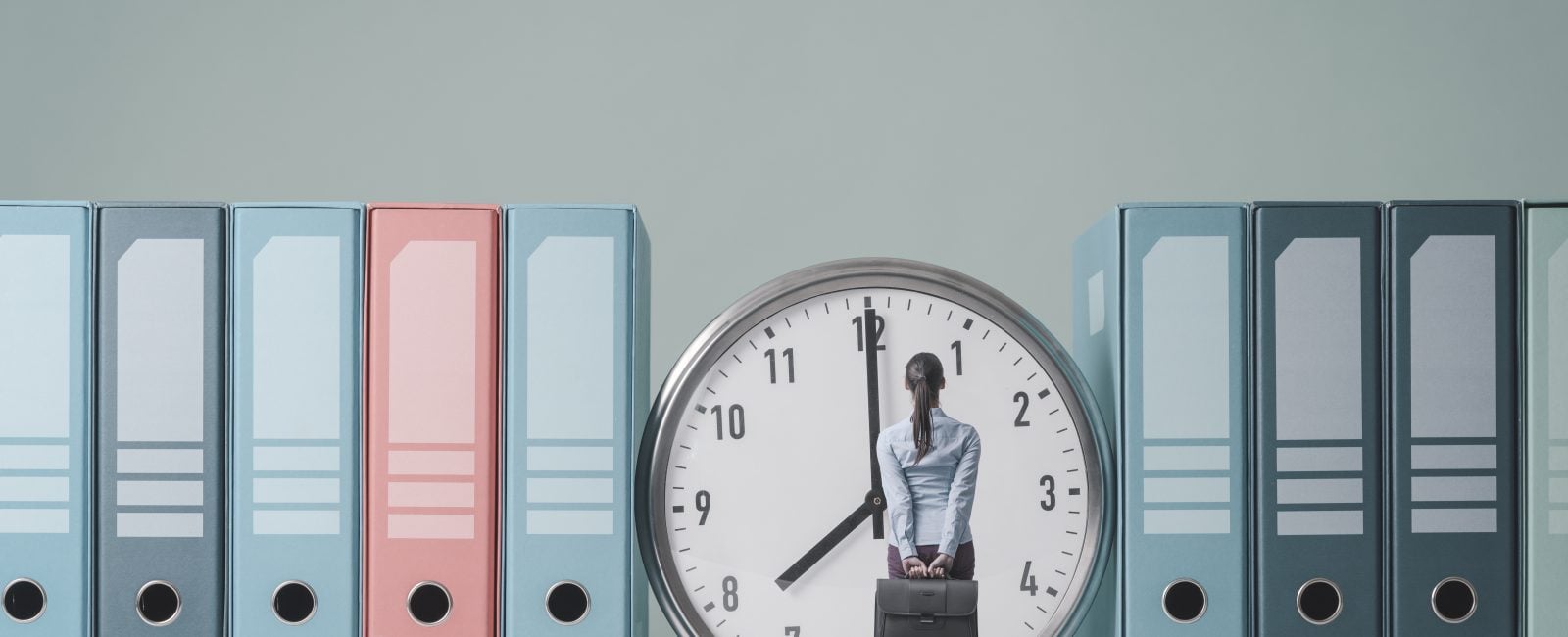 Businesswoman holding her briefcase and checking the time on a huge clock, she is standing and waiting