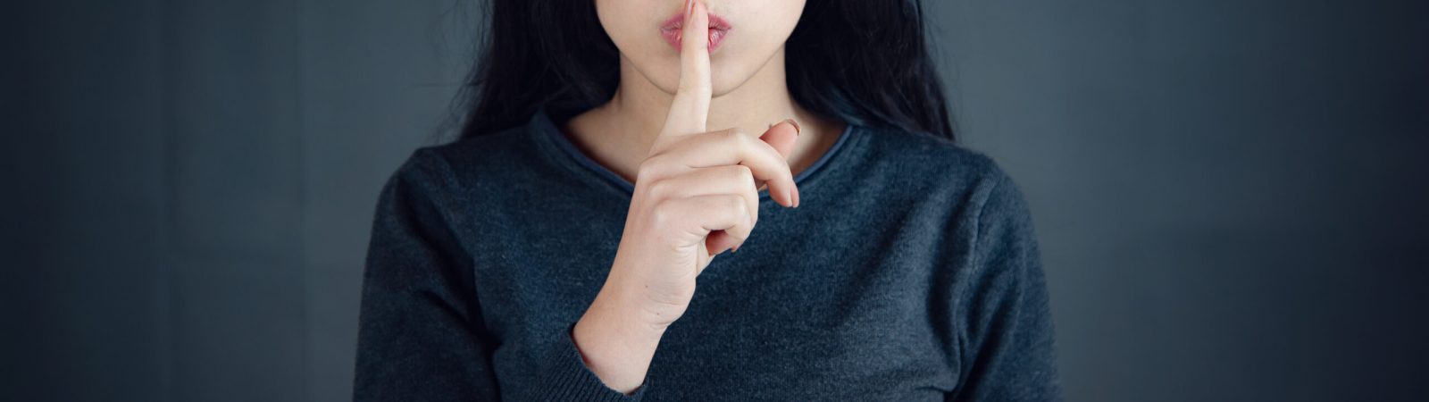 Woman showing a sign of silence gesture putting finger in mouth.