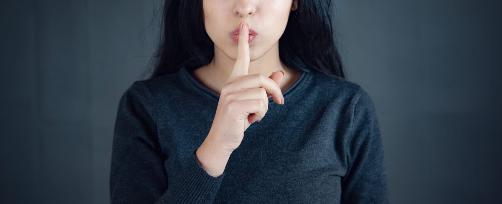Woman showing a sign of silence gesture putting finger in mouth.