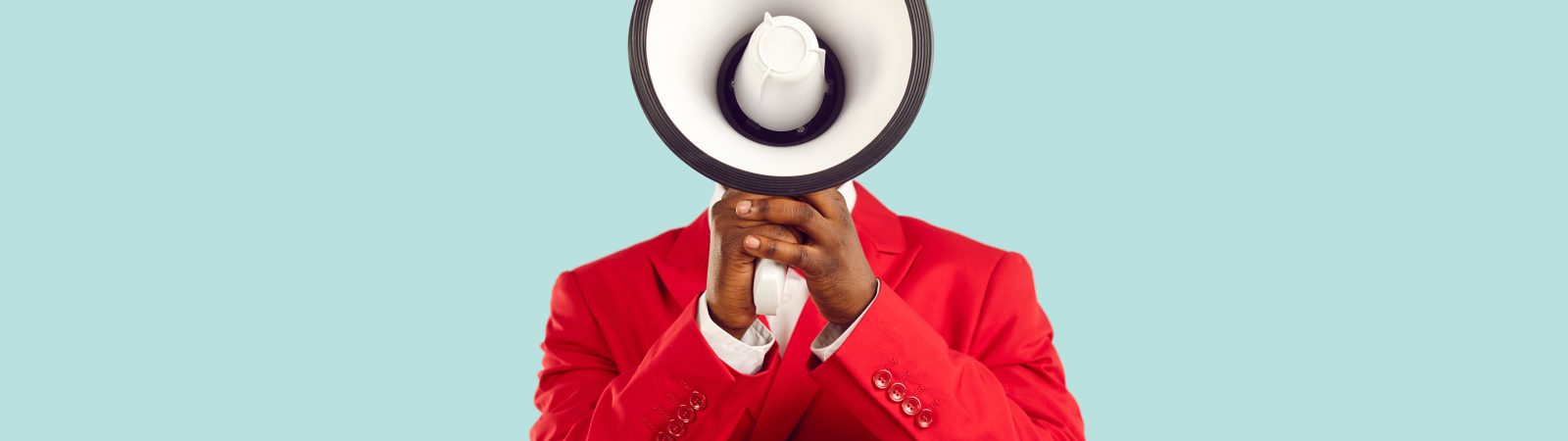 Dark-skinned man hiding his face behind loudspeaker makes loud advertisement on pastel light blue background. Unknown man in red elegant jacket loudly announces crazy discounts. Advertisement concept.