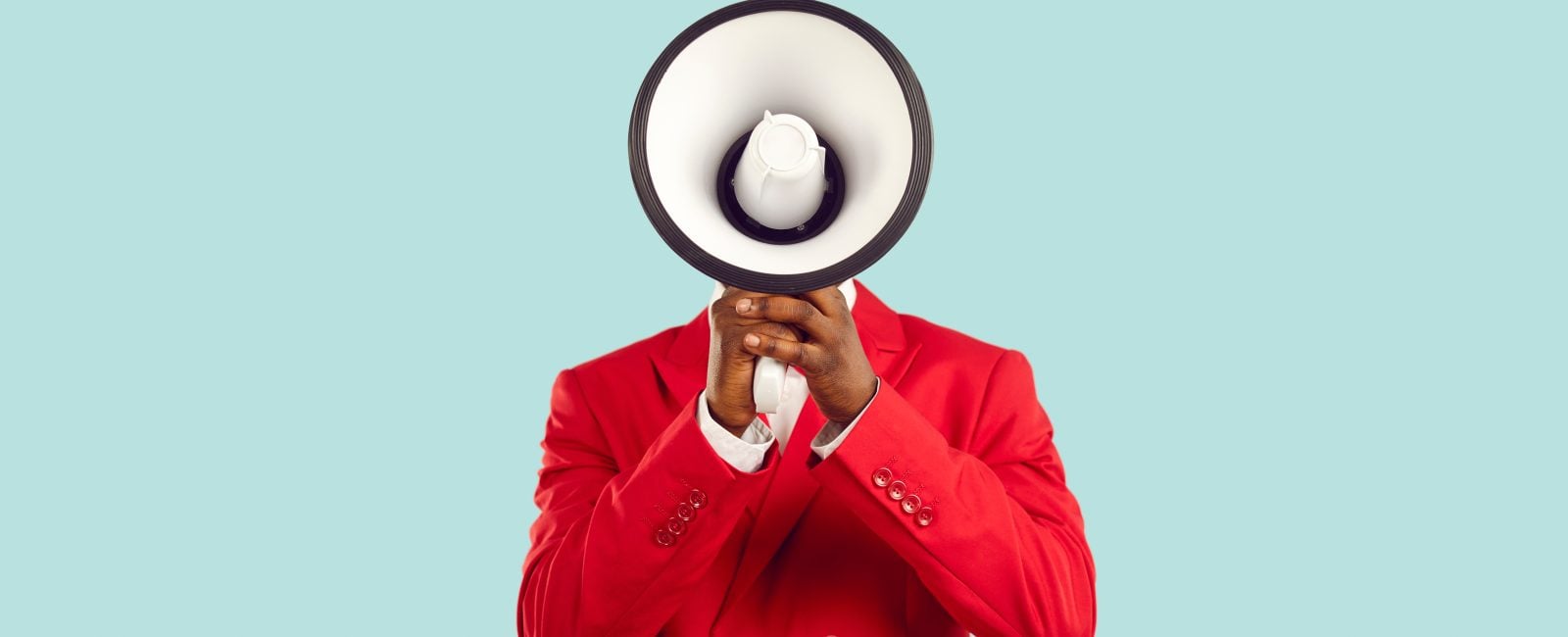 Dark-skinned man hiding his face behind loudspeaker makes loud advertisement on pastel light blue background. Unknown man in red elegant jacket loudly announces crazy discounts. Advertisement concept.