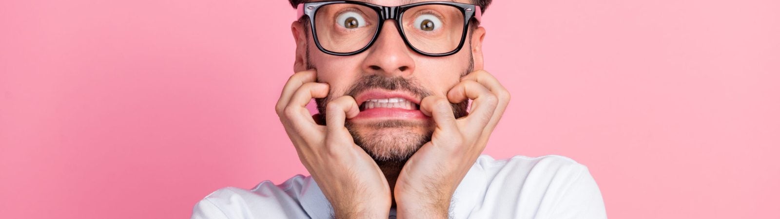 Closeup photo of young funnny handsome attractive bearded man bite fingers nails nervous face wear glasses deadline work manager isolated on pink color background.