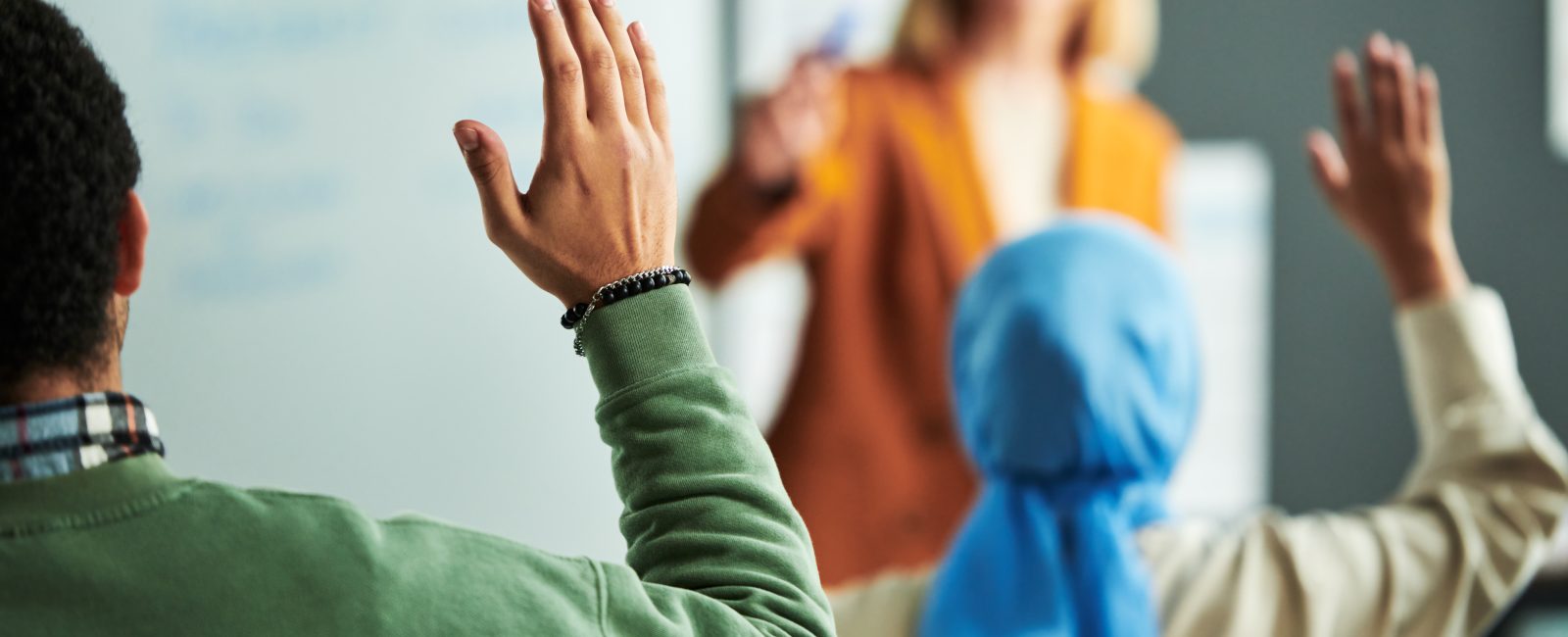 Raised hand of student working at seminar while sitting in front of speaker and young Muslim female learner in blue hijab