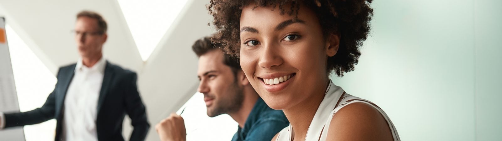 Cheerful businesswoman. Young afro american woman is looking at camera and smiling while her boss standing near whiteboard and discussing something with team. Teamwork. Meeting
