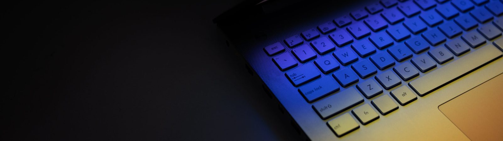 closeup of laptop computer keyboard on dark table with colorful light reflection. banner with copy space