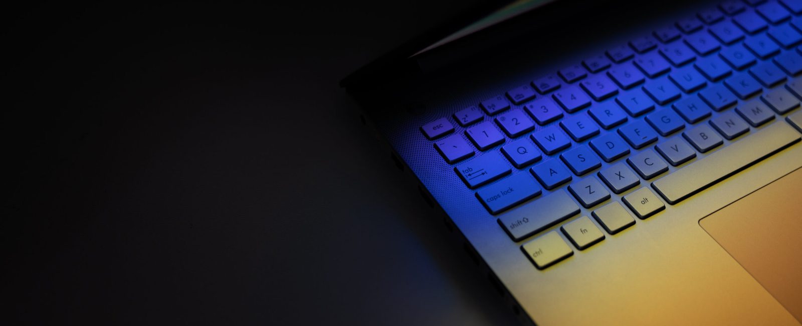closeup of laptop computer keyboard on dark table with colorful light reflection. banner with copy space