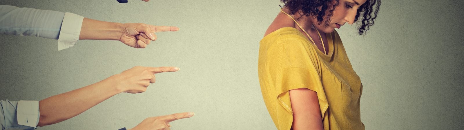 Concept accusation guilty person girl. Side profile sad upset woman looking down many fingers pointing at her back isolated grey office wall background. Negative human face expression emotion feeling