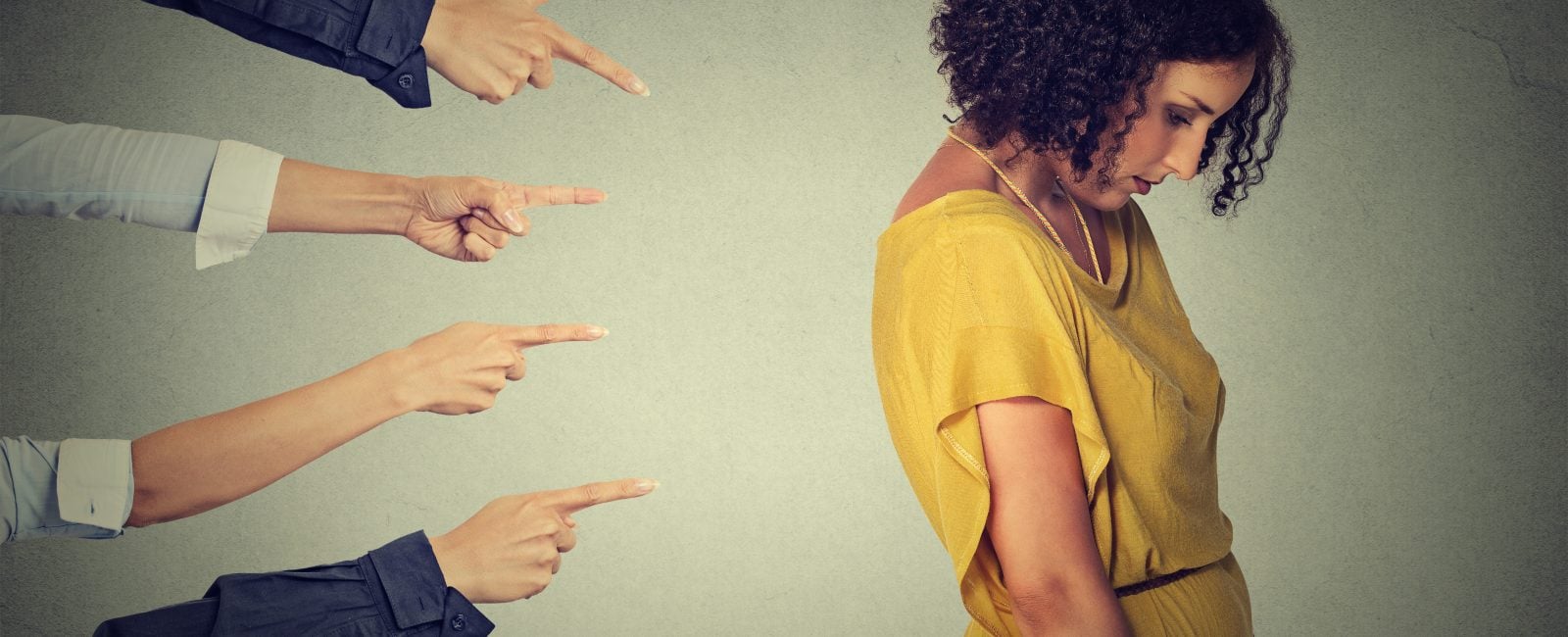 Concept accusation guilty person girl. Side profile sad upset woman looking down many fingers pointing at her back isolated grey office wall background. Negative human face expression emotion feeling